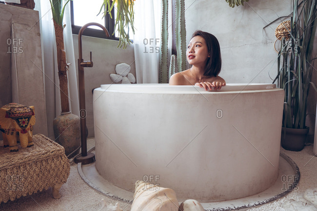 Happy young Asian woman enjoying bath time in bathtub in hotel room with traditional oriental decor while spending holidays in Taiwan
