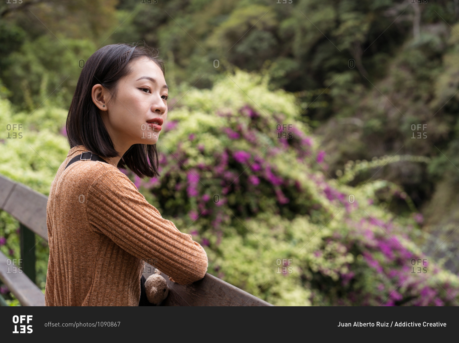 Asian female tourist standing on wooden terrace enjoying summer vacation in green park in Hualien City and looking away