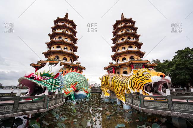 Low angle exterior of traditional oriental pagodas with colorful ornamental Tiger and Dragon sculptures built on lake and connected with shore by stone bridges in Kaohsiung city in Taiwan