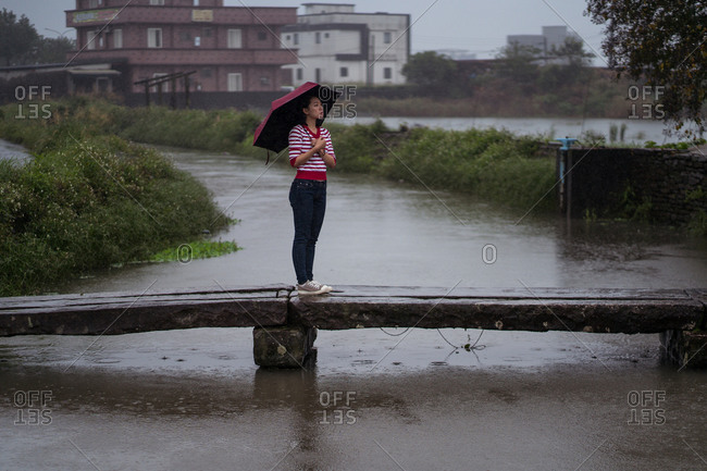 Side view of female with umbrella walking along wooden footbridge while enjoying solitude on rainy day in Yilan county and looking away