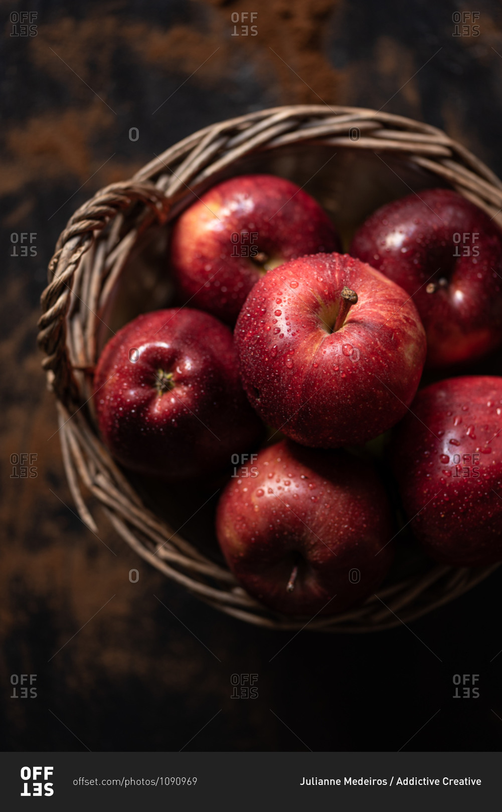 Top view of pile of wet red apples placed in wicker basket on rustic table