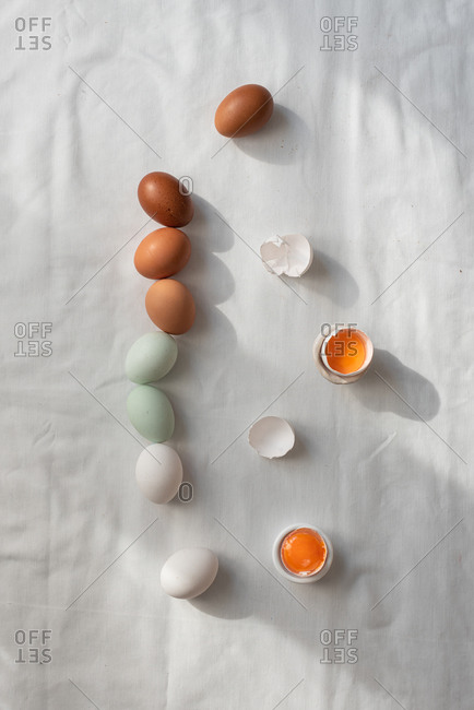 From above of colorful raw eggs placed in row on white table in kitchen