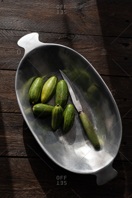 From above of ripe delicious cucumbers in metal bowl placed on rustic table in kitchen