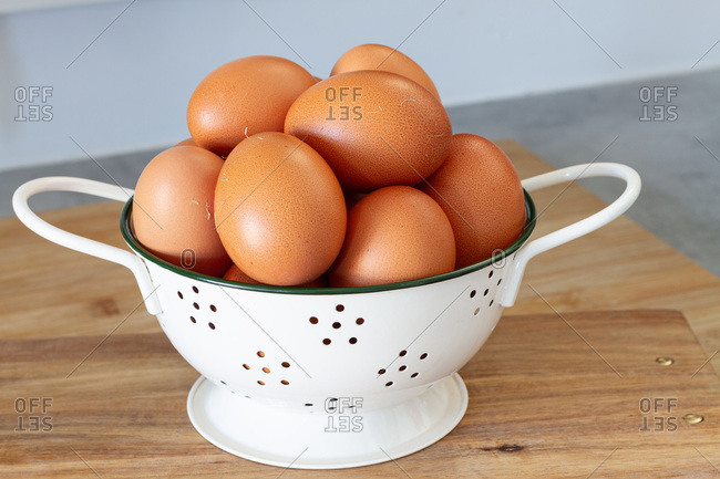 Heap of brown chicken eggs in white colander placed on table in cozy home kitchen