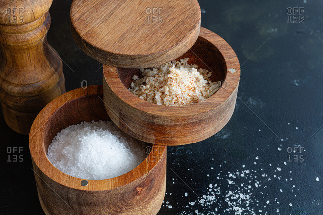 High angle of assorted types of salt in wooden jars placed on table with pepper mill in kitchen