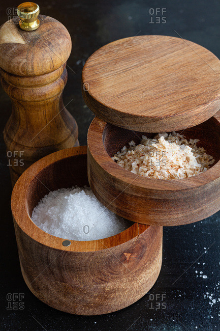 High angle of assorted types of salt in wooden jars placed on table with pepper mill in kitchen