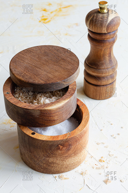 Top view of various types of salt in wooden jars and spoons placed on white table in kitchen