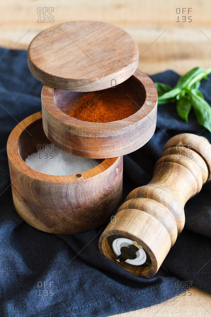 High angle of wooden pepper mill and jars with salt and aromatic paprika arranged on napkin on table in domestic kitchen