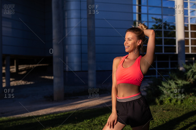 Positive female runner in sportswear standing in city and looking away