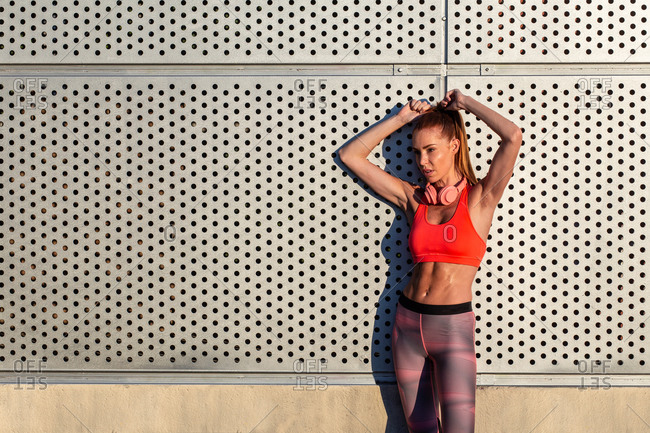 Female athlete in sportswear standing near building in city and relaxing after workout in summer on sunny day