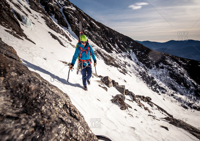 Climber walking through rocks on side of snowy mountain