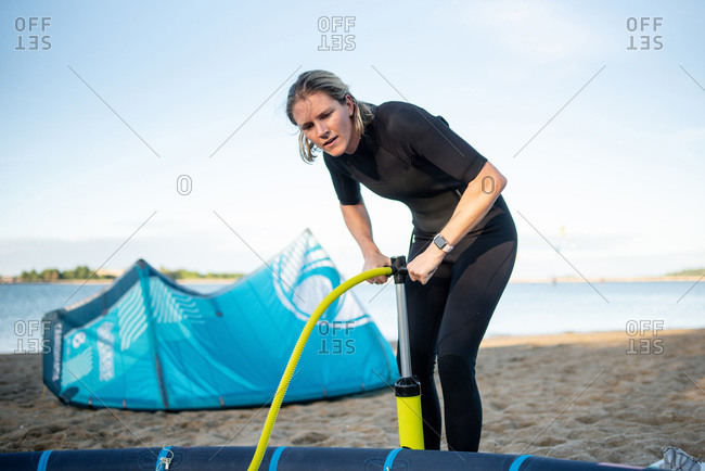 A woman in wetsuit pumps up a kiteboarding kite on a beach