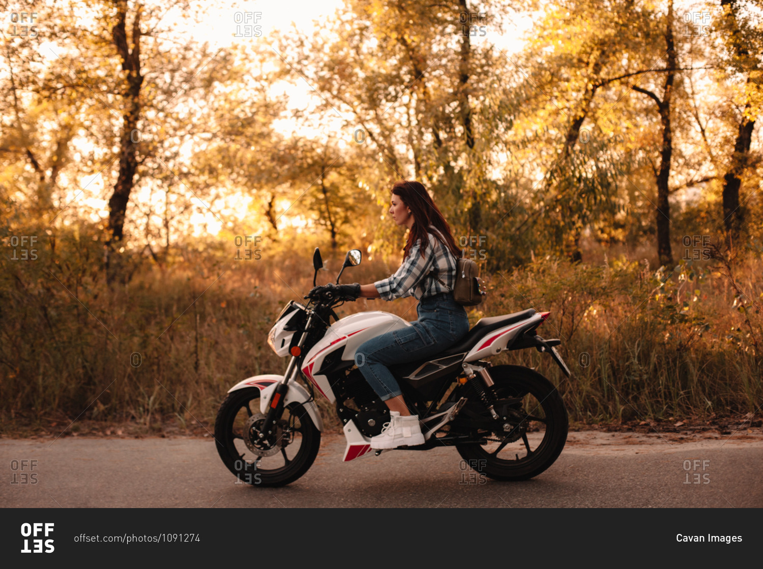 Young confident woman riding motorcycle on country road at sunset