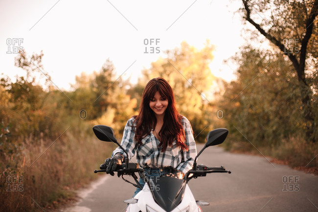 Portrait of happy young woman sitting on motorcycle on country road
