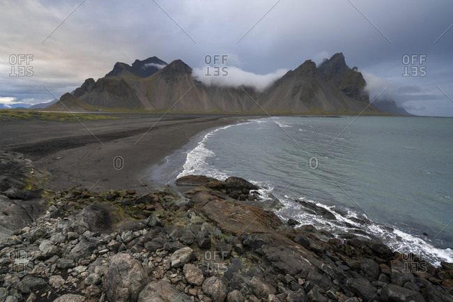 Scenic view of vestrahorn mountain range by sea against cloudy sky at stokksness, iceland