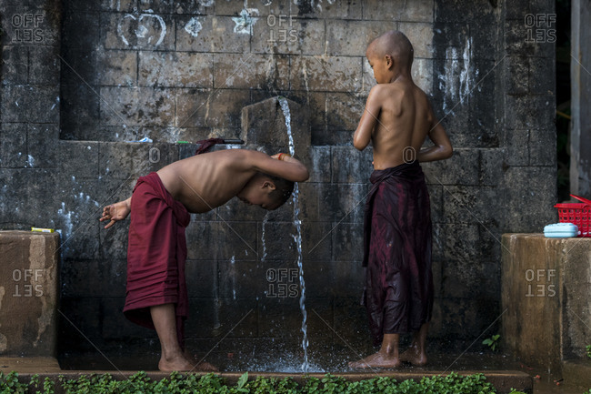 Hsipaw, shan, myanmar (burma) - january 15, 2018: novice shirtless monks bathing under running water outdoors, near hsipaw, myanmar