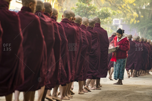 Nyaung-u, mandalay region, myanmar (burma) - january 18, 2018: burmese woman giving steamed rice to monks standing in line, nyaung u, myanmar