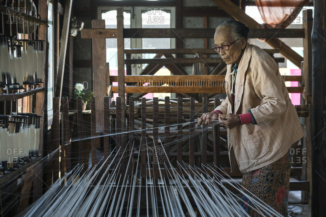 Nyaungshwe, shan, myanmar (burma) - january 20, 2018: senior burmese woman preparing threads to work on loom, lake inle, myanmar