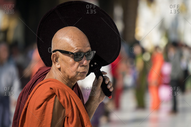 Yangon, yangon region, myanmar (burma) - january 28, 2018: buddhist monk dressed in saffron robe wearing sunglasses and holding hand fan during sunny day, shwedagon pagoda complex, yangon, myanmar