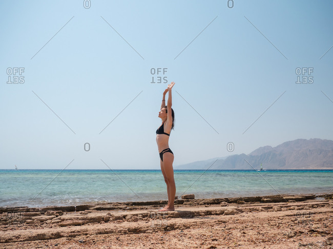 Young brunette woman doing exercises on the beach near sea