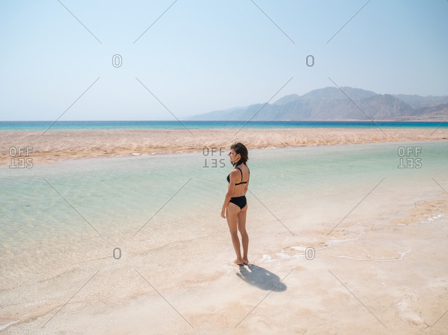 Young brunette woman relaxing on the beach near sea and mountains
