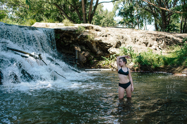 Portrait of teen girl standing in knee deep river near a waterfall
