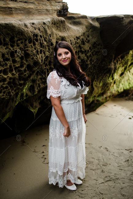 Newlywed bride standing between rocks on beach in san diego