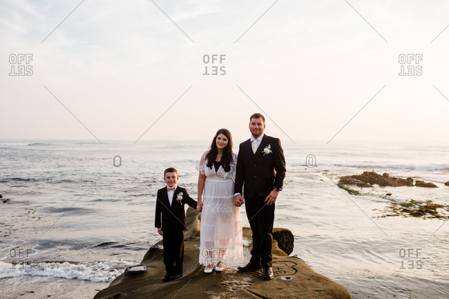 Newlyweds & nine year old son standing on rock at beach in san diego