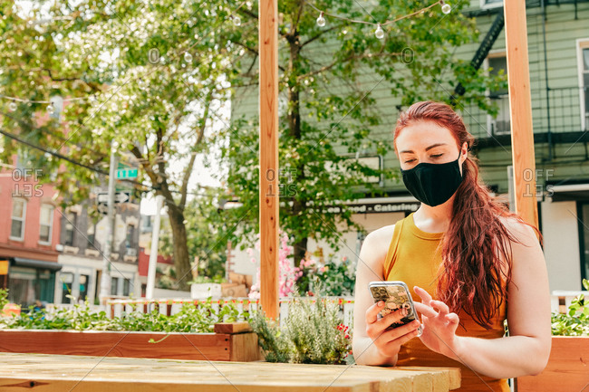 Young woman sitting in an outdoor restaurant table, wearing face mask.