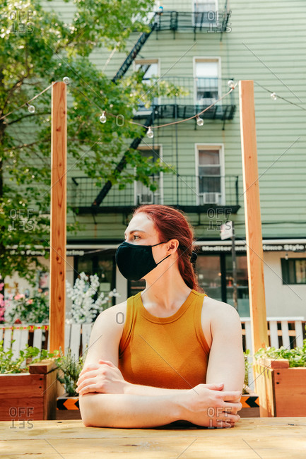 Young woman sitting in an outdoor restaurant table, wearing facemask.