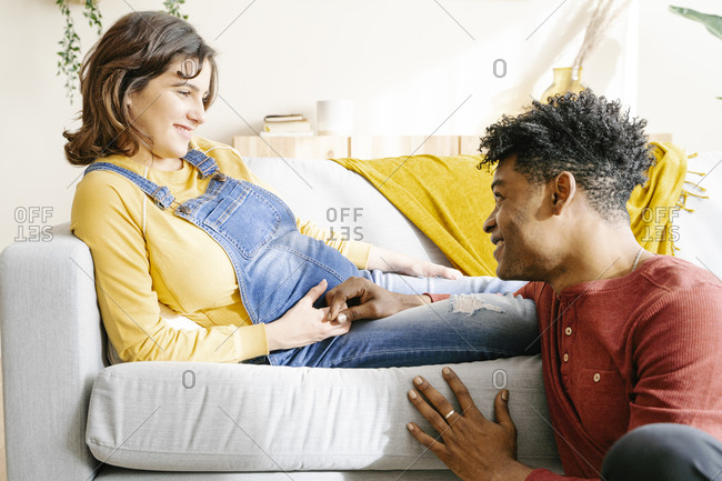 Husband stroking the belly of his pregnant wife on a sofa. interracial couple concept