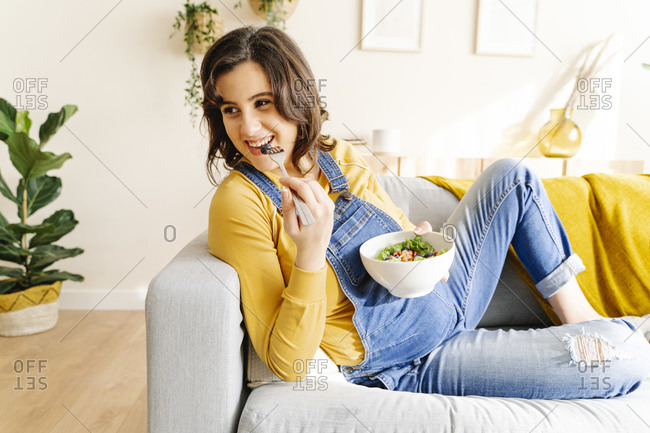 Young woman pregnant and eating a salad on a sofa. maternity concept