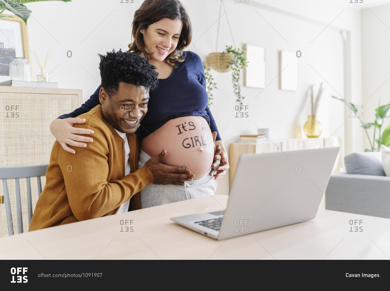 Husband and pregnant wife celebrating ultrasound results in front of a laptop, with a phrase written on her belly that it is a girl. parenthood concept