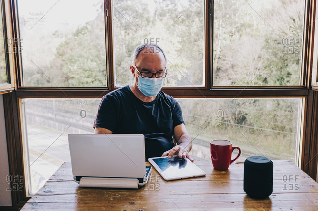 Mature man with mask working on laptop at home