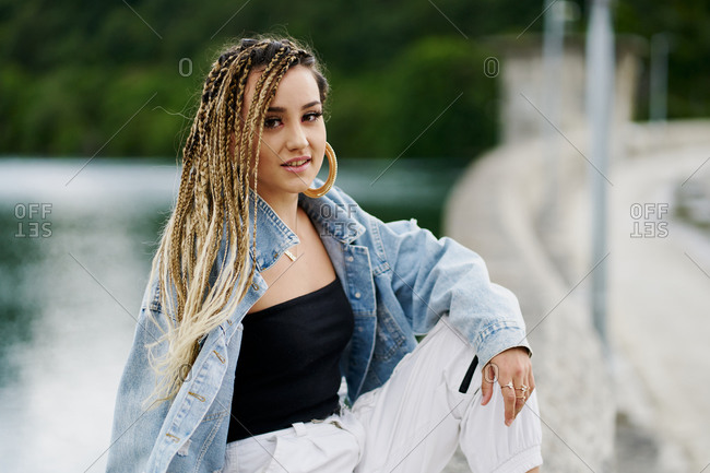 Portrait of young woman with braided hair wearing a denim jacket sitting on a bridge