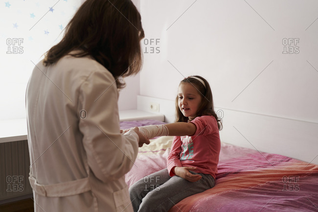 Female doctor bandaging the arm of a little girl in her room. home doctor concept