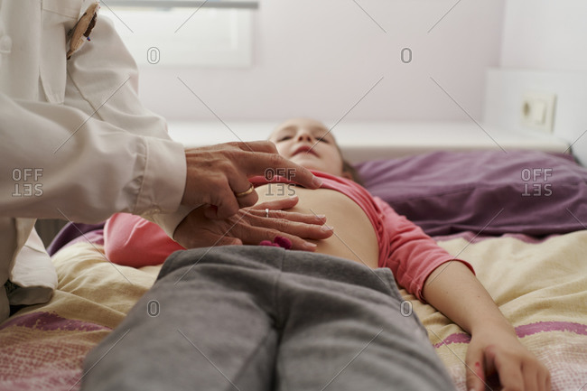 Female doctor examining a little girl's abdomen in her room. home doctor concept