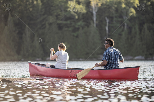 African american man and woman paddle canoe on beautiful lake in maine
