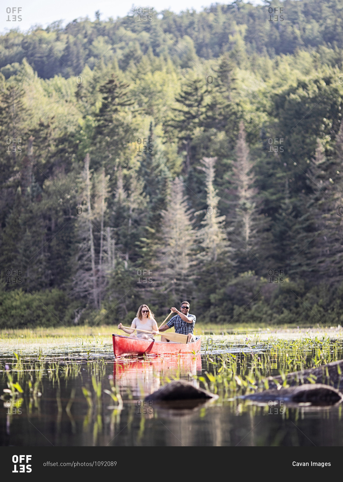 Couple, white woman and black male paddle in red canoe on lake, maine