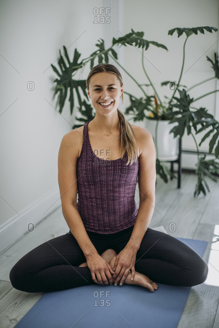 Smiling yoga instructor in home studio sitting cross-legged on yoga mat