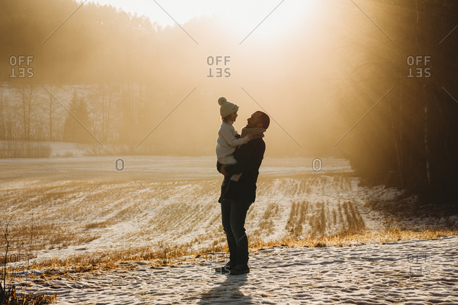 Father holding daughter up in golden field during sunset in winter