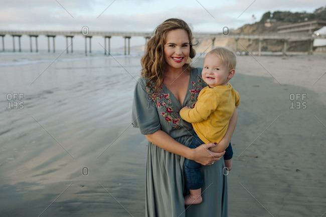 Beautiful 30 yr old mom holding baby at beach with pier in background