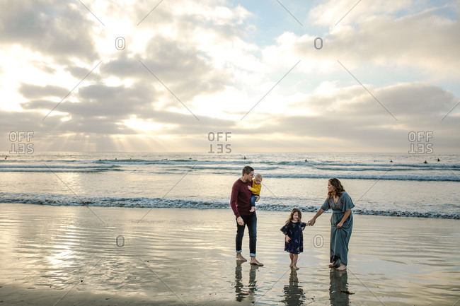 Barefoot young family wading in the ocean surf at sunset