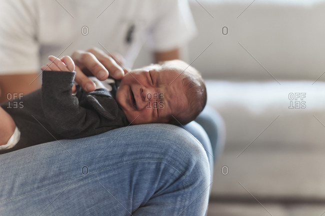 Newborn baby fussing while lying in mother's lap and father's hand is trying to comfort him