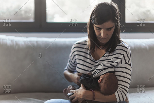 Mother sitting on sofa breastfeeding her newborn baby