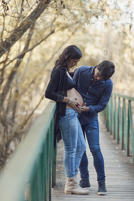 Couple embracing woman's pregnant belly on a footbridge in autumn