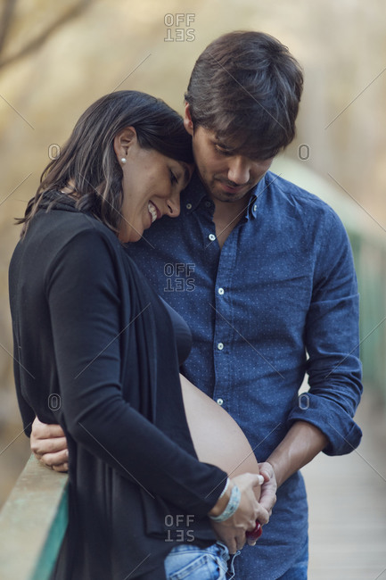 Couple embracing while touching the woman's pregnant belly outdoors