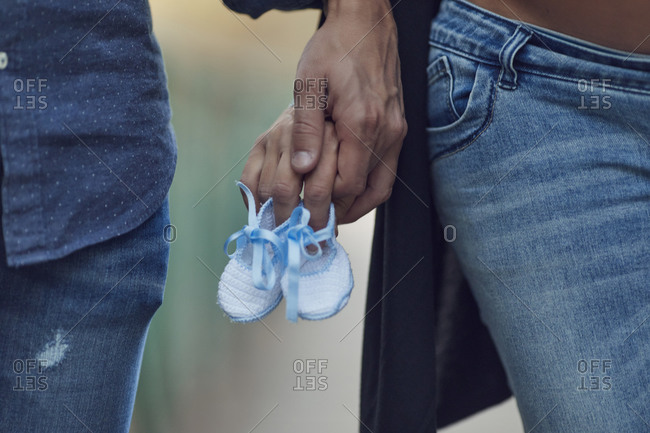 Pregnant couple holding hands and newborn baby booties