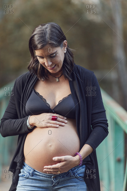Woman standing on footbridge looking down at her pregnant belly in fall