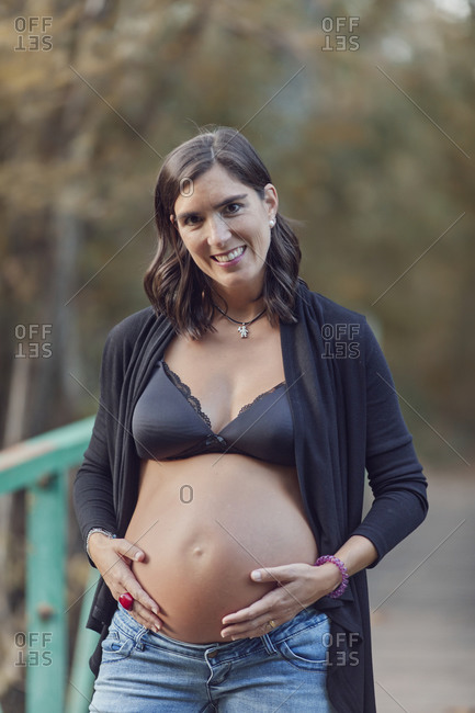 Pregnant woman standing on footbridge holding her pregnant belly in fall